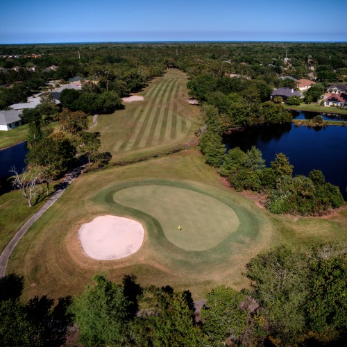 Aerial view of the golf course. A bunker sits on the left edge of the green. A lake to the right.