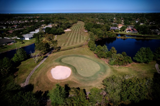 Aerial view of the golf course. A bunker sits on the left edge of the green. A lake to the right.
